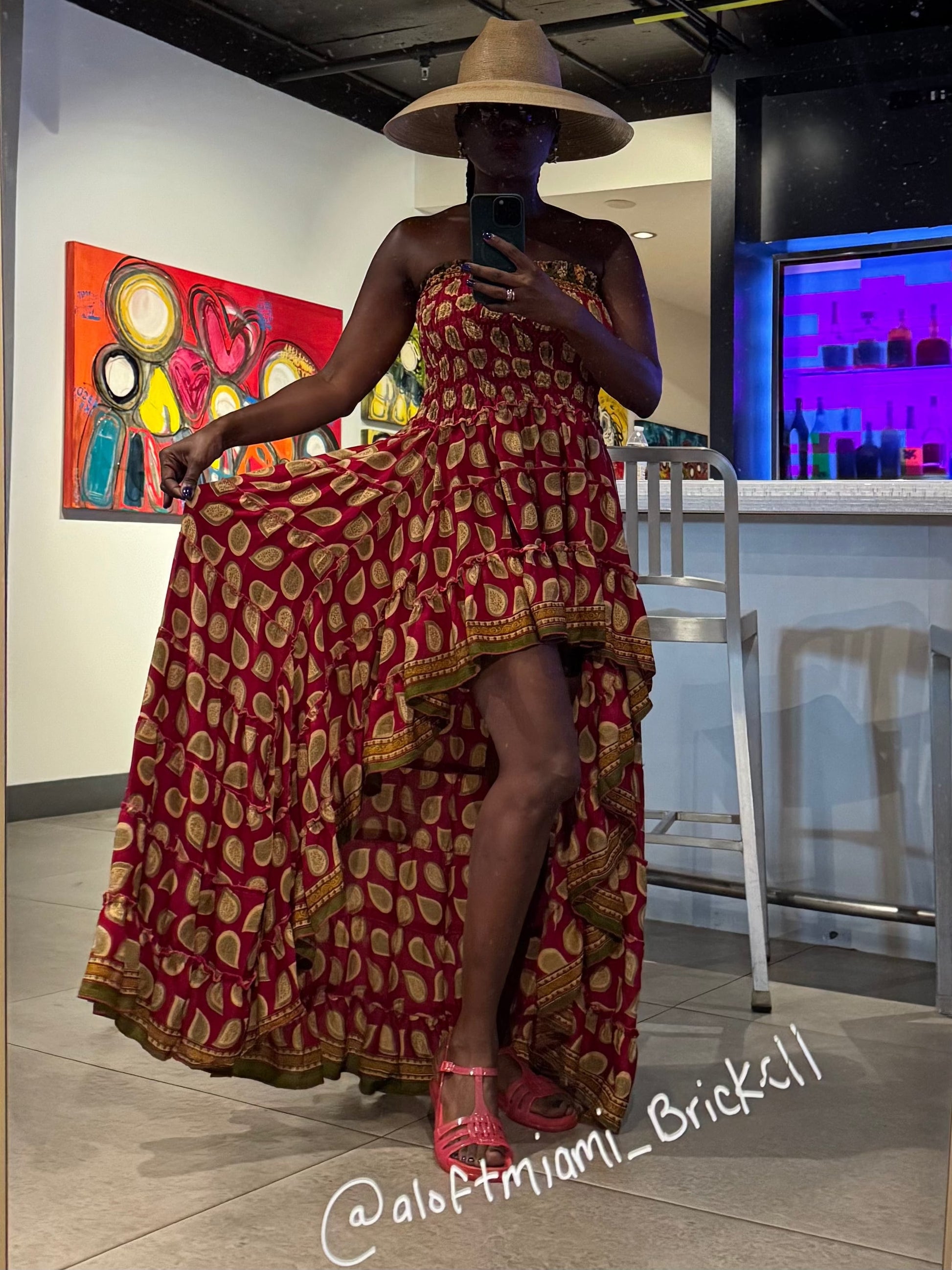 Person wearing a red and gold patterned dress taking a mirror selfie in a modern indoor setting.